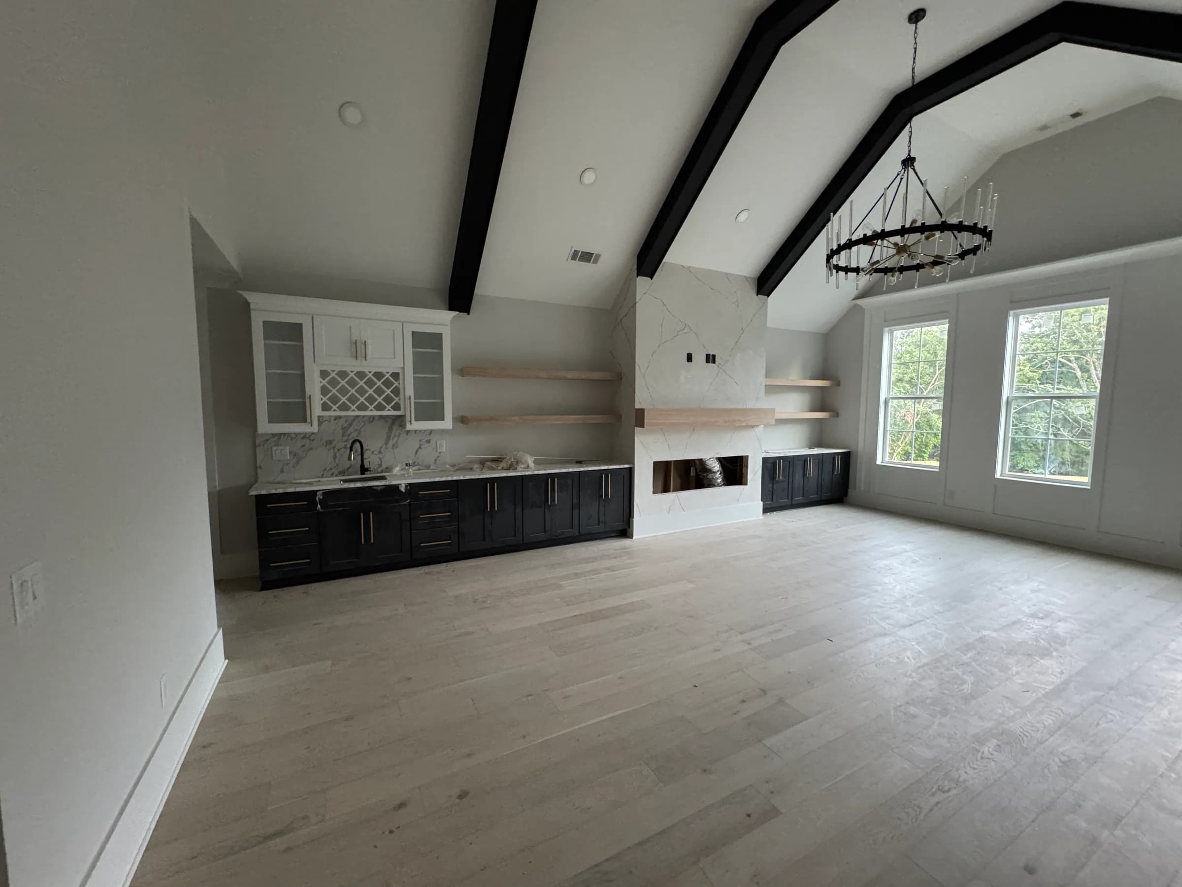 Vaulted great room with black bar cabinetry, floating oak shelves and marble fireplace surround